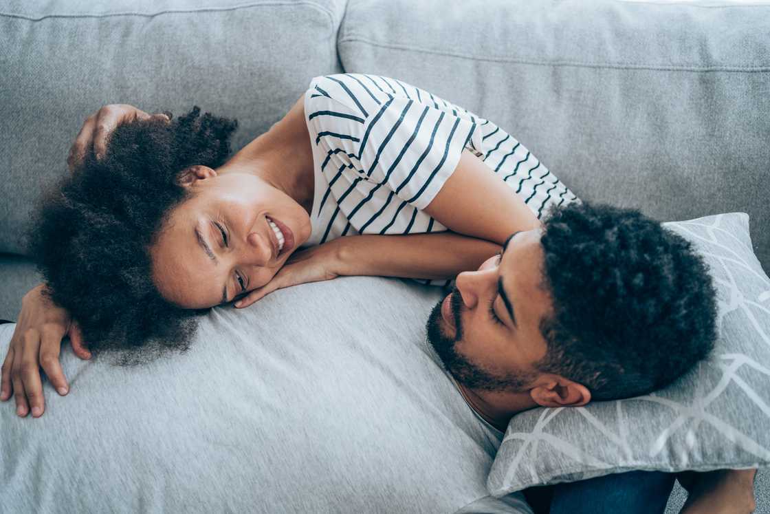 A young couple lying together on their sofa at home.