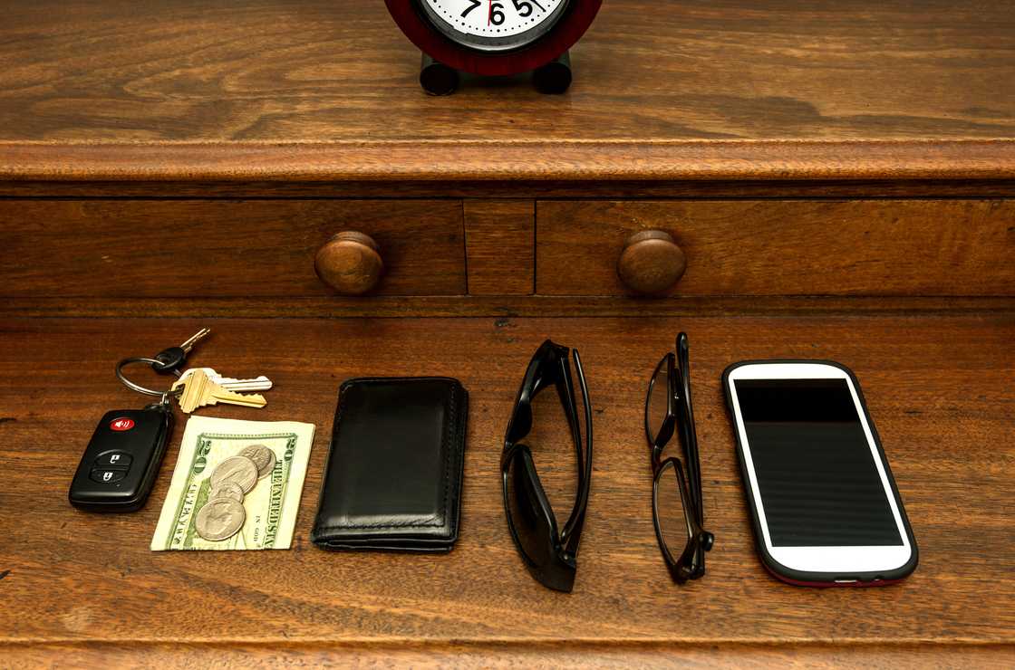 A phone, wallet, shades, car keys, and money on top of a dresser A phone, wallet, shades, car keys, and money on top of a dresser