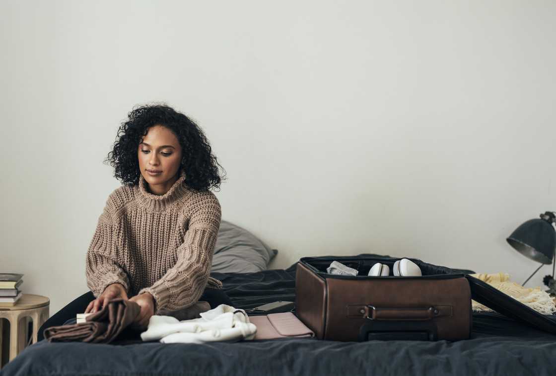 A woman folds clothes beside an open suitcase on a bed.