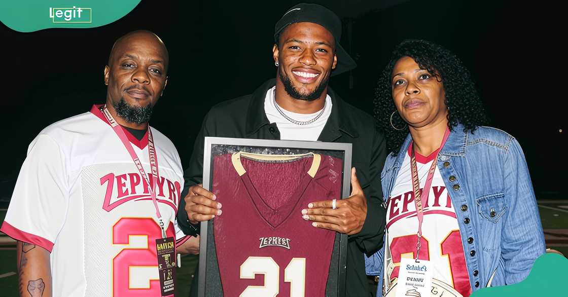 Saquon Barkley poses standing his parents while holding his retired high school jersey Saquon Barkley poses standing his parents while holding his retired high school jersey