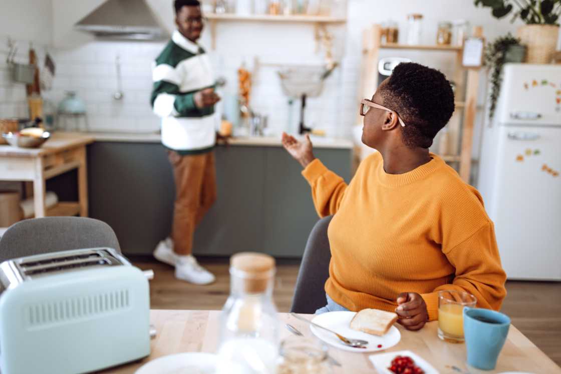 A young man in pyjamas arguing with his mother over breakfast.