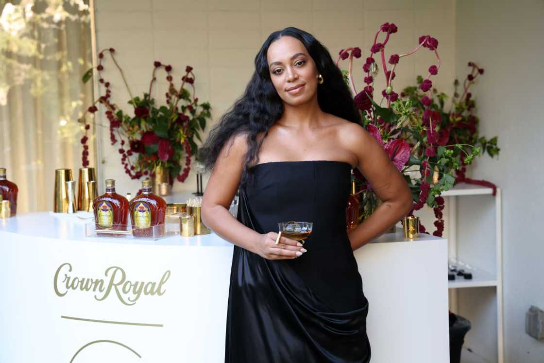 Solange Knowles poses in a black dress holing a drink