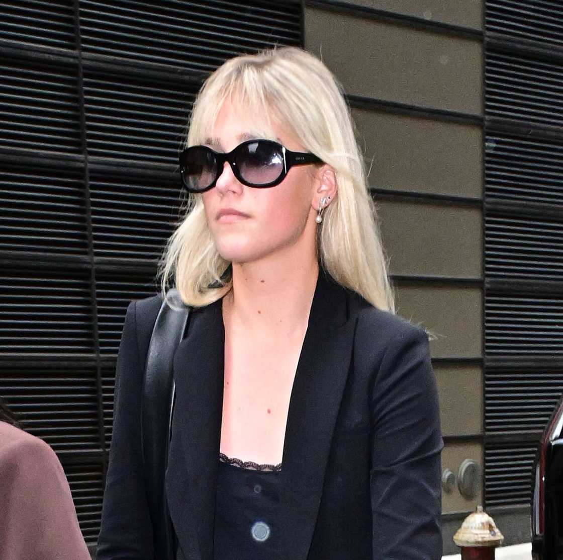 Ashleigh Scully walks outdoors wearing sunglasses, a black blazer, and a lace-trimmed top.