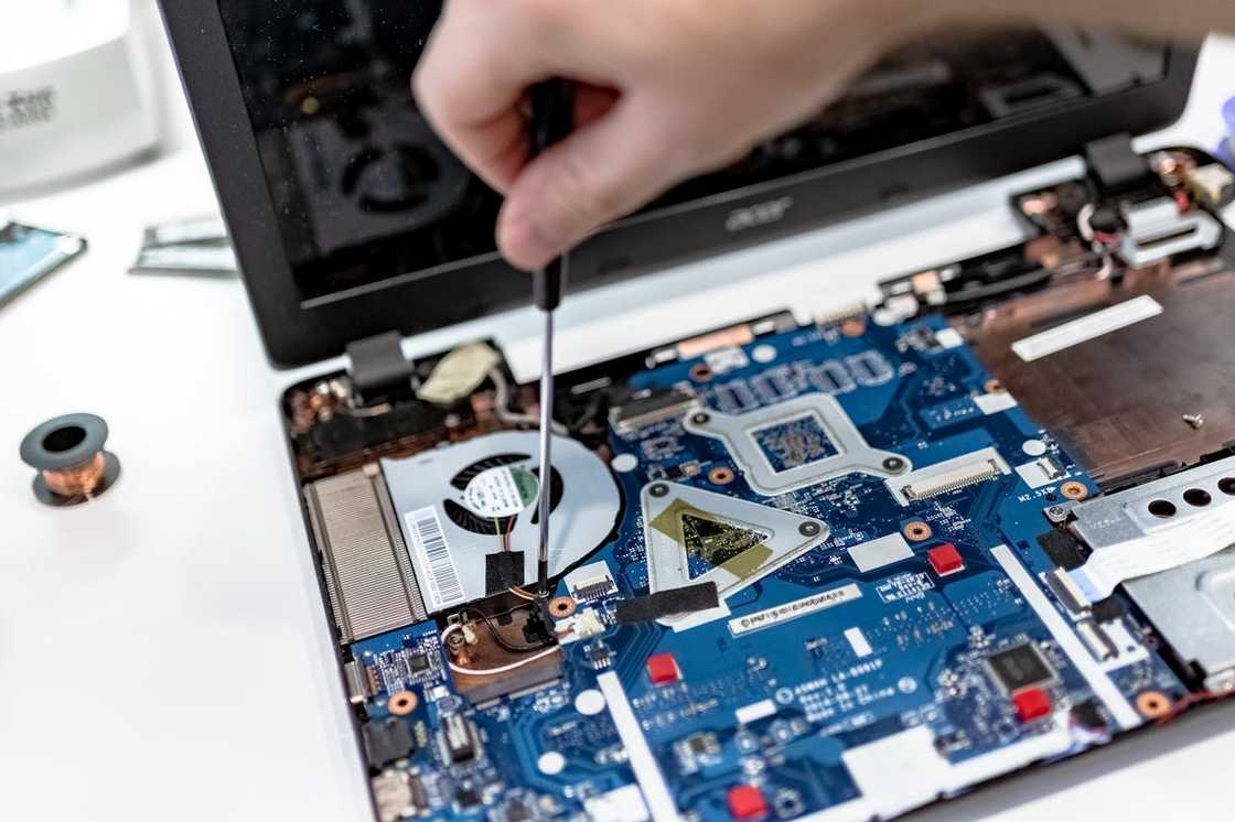 Hand using a screwdriver to repair an open laptop motherboard.