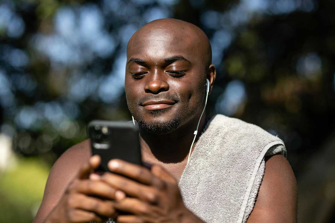 A man listening to music from a smartphone while earing earphones A man listening to music from a smartphone while earing earphones