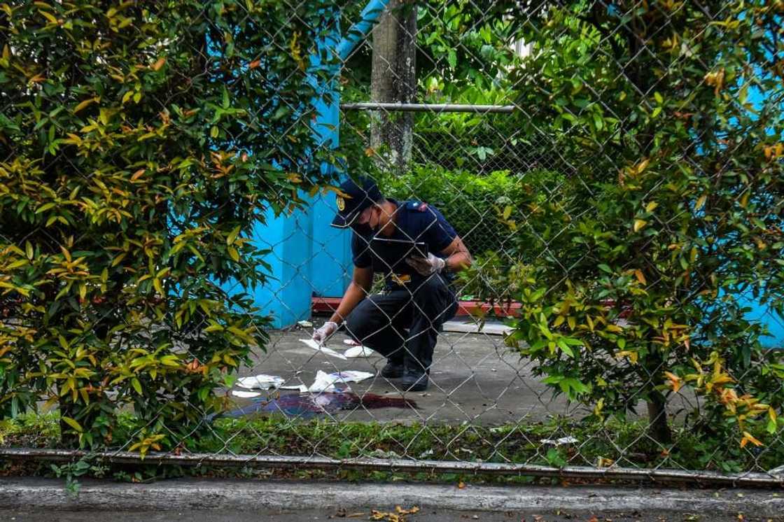 A police officer collects evidence by a pool of blood after three people were killed in a shooting at Ateneo de Manila University in Manila