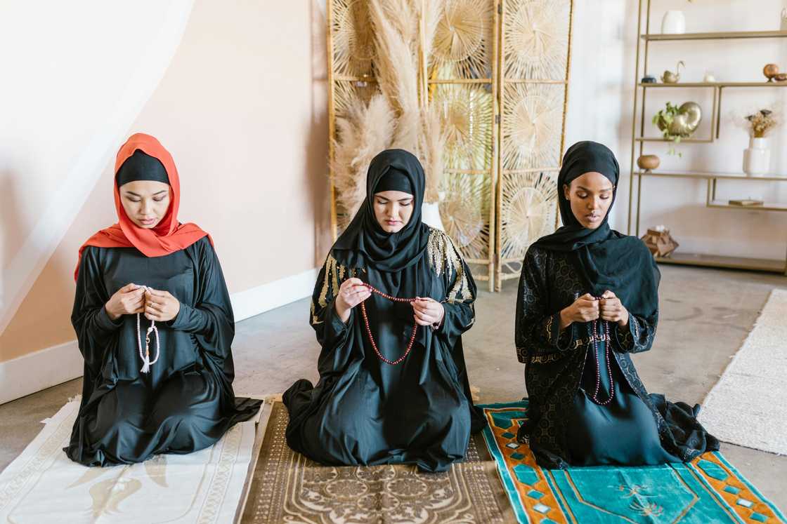 Three Muslim women kneeling on prayer mats as they say dua