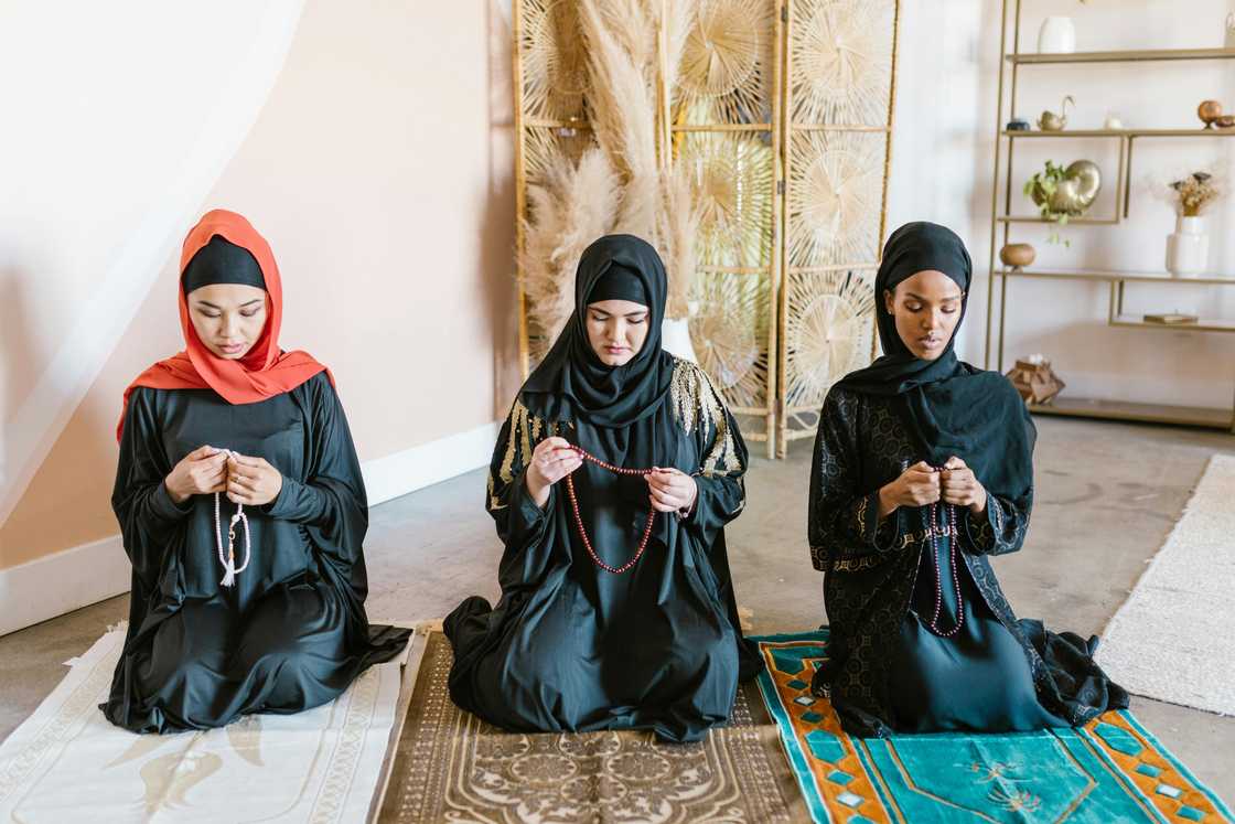 Three Muslim women kneeling on prayer mats as they say dua Three Muslim women kneeling on prayer mats as they say dua