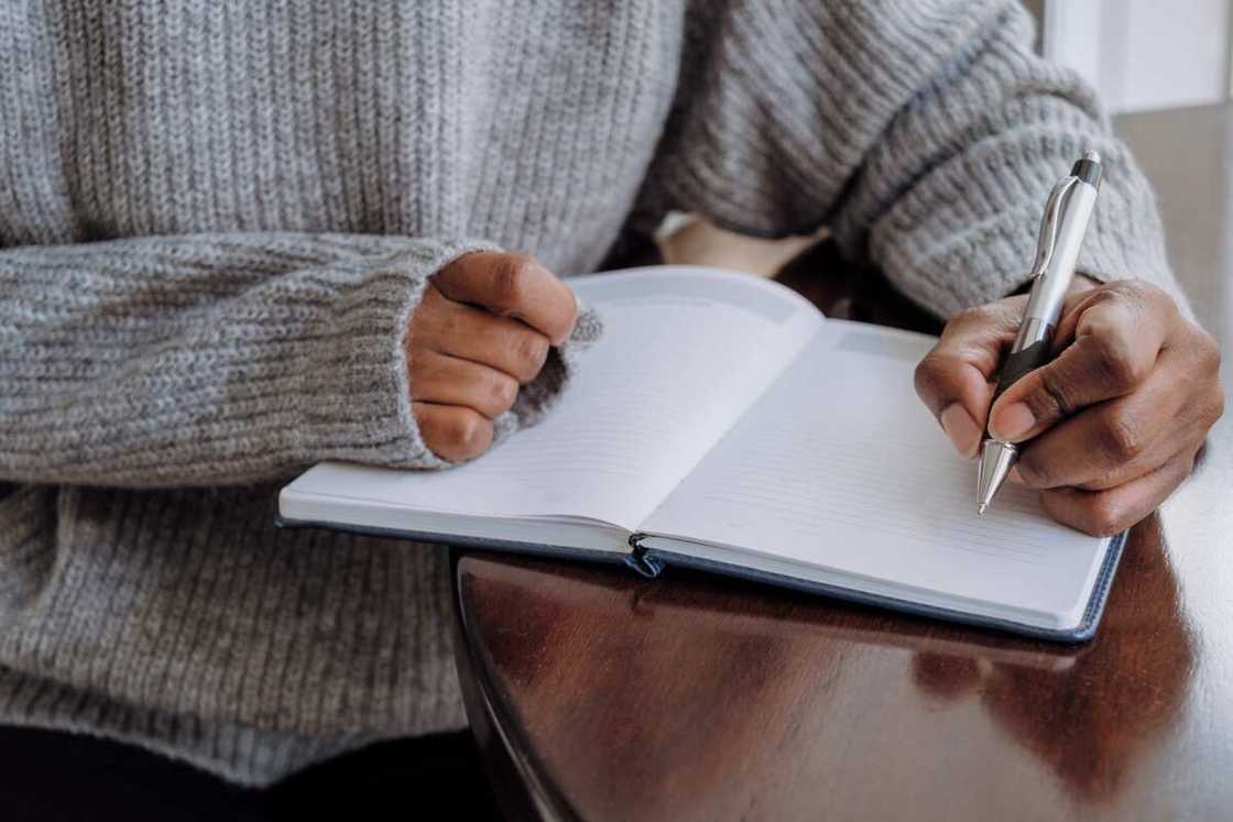 Close-up of an unrecognisable woman writing in a journal while sitting at the table Close-up of an unrecognisable woman writing in a journal while sitting at the table