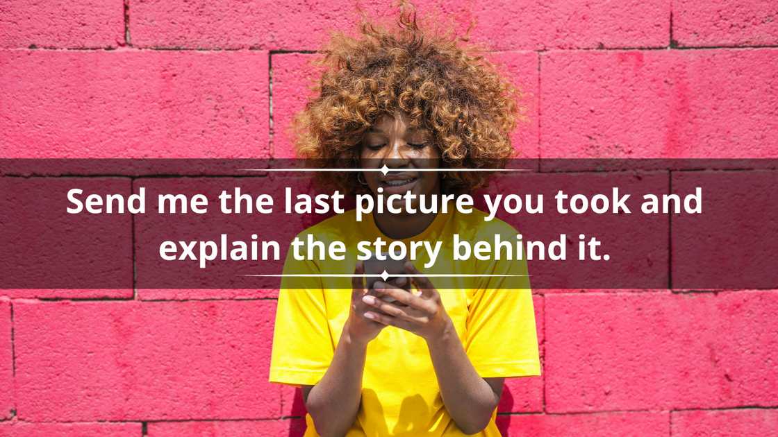A happy woman in a yellow tee is texting on a smartphone in front of a pink brick wall A happy woman in a yellow tee is texting on a smartphone in front of a pink brick wall