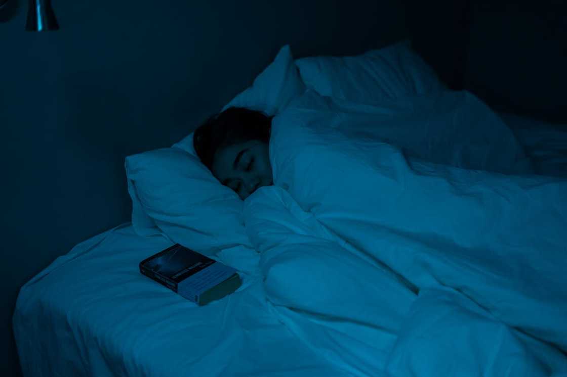 A person sleeps in bed at night with a phone lying nearby. A person sleeps in bed at night with a phone lying nearby.