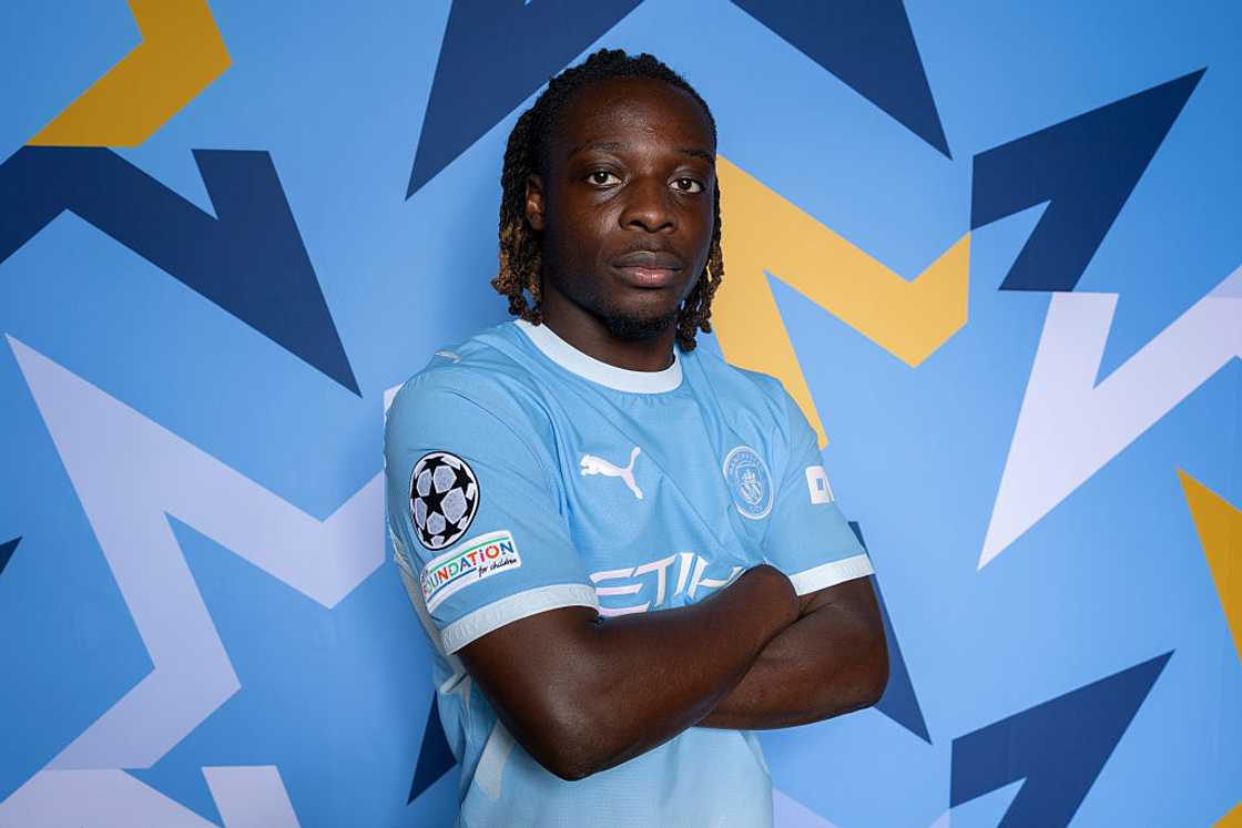 Jeremy Doku, in the sky-blue Manchester City home kit, poses with arms folded against a blue patterned backdrop at the club's Champions League 2026/27 portrait session in Manchester on 19 August 2026. Jeremy Doku, in the sky-blue Manchester City home kit, poses with arms folded against a blue patterned backdrop at the club's Champions League 2026/27 portrait session in Manchester on 19 August 2026.