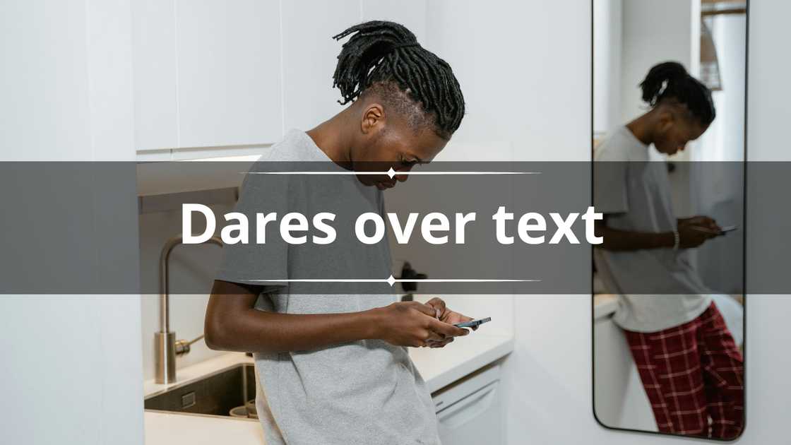 A man in a grey tee and checkered pants is texting in front of a mirror A man in a grey tee and checkered pants is texting in front of a mirror