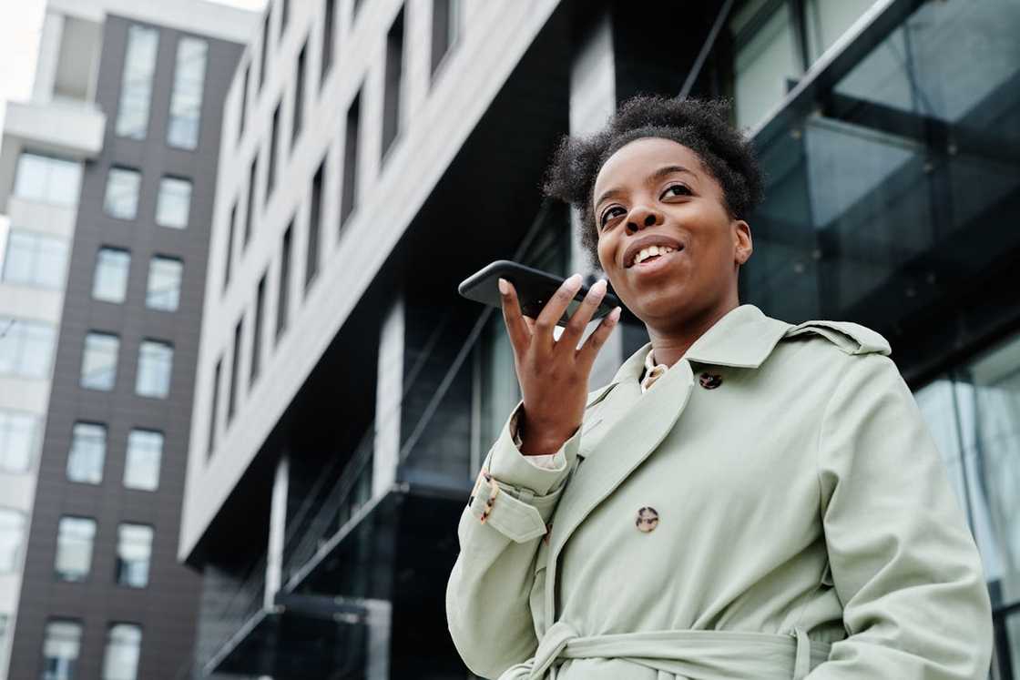 A woman speaks into a smartphone outside a modern office building. A woman speaks into a smartphone outside a modern office building.