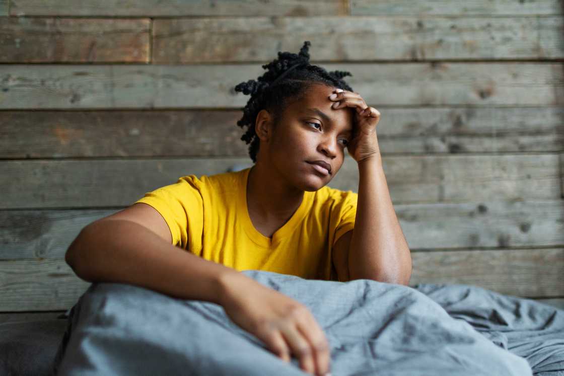 A worried young adult black woman sitting in bed A worried young adult black woman sitting in bed