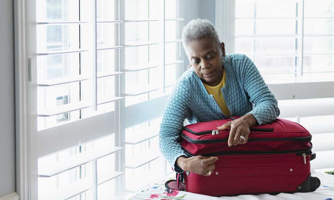 A n elderly woman packs clothes into a suitcase.