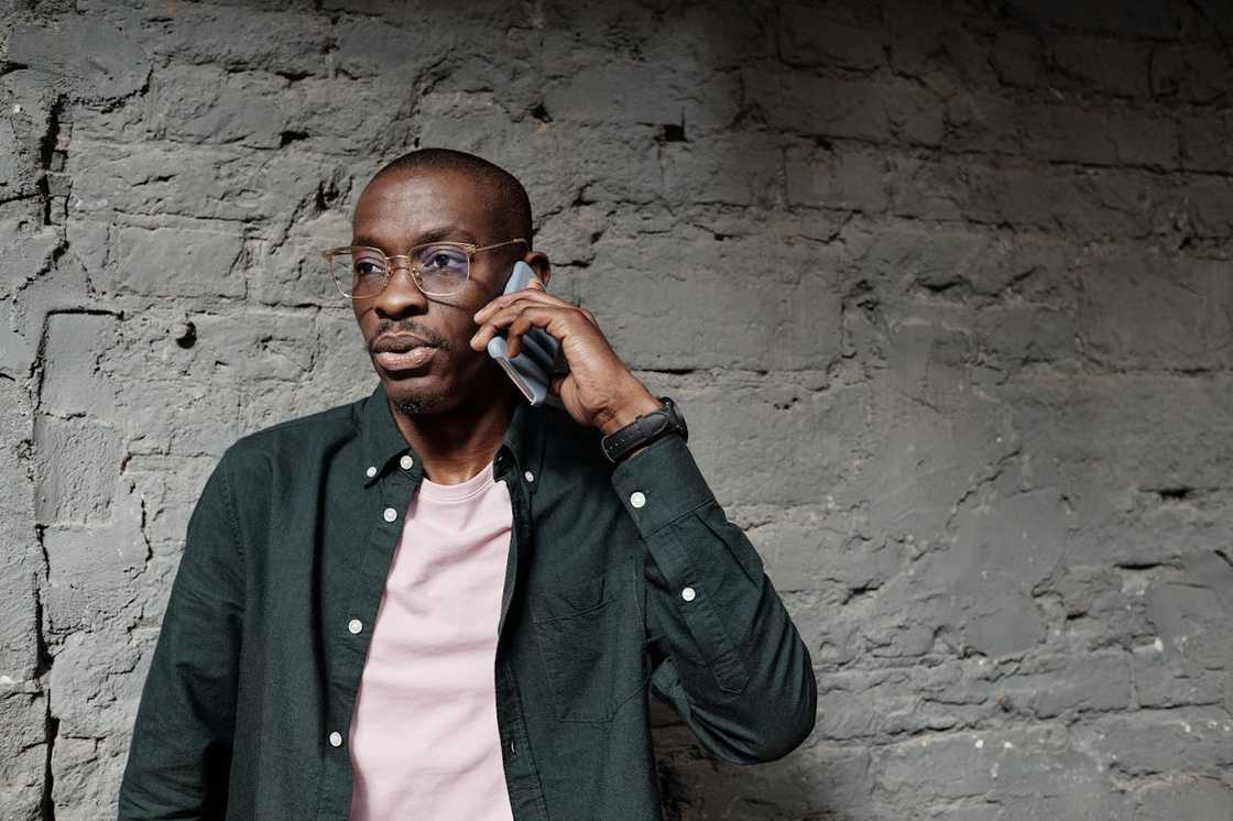 A concerned man talks on a phone while standing against a brick wall.