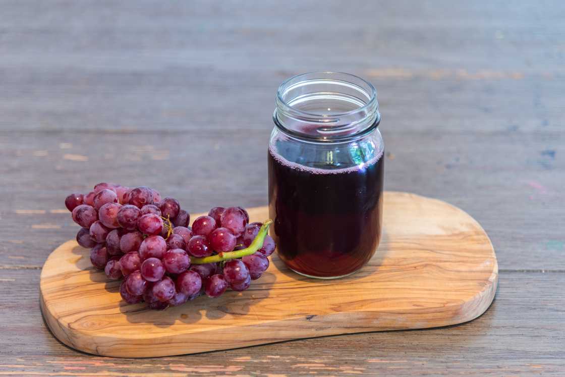 Grape drink in jar on cutting board with grapes on rustic wood table Grape drink in jar on cutting board with grapes on rustic wood table