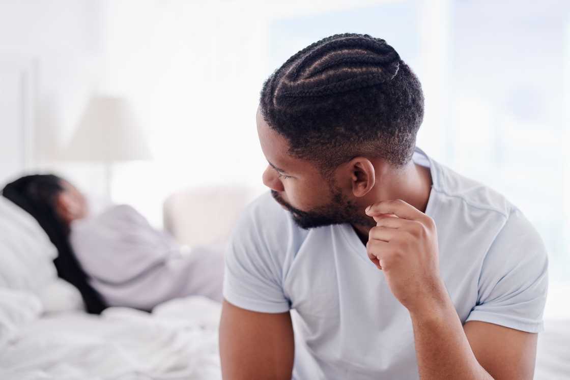 A man sitting on the bed while his girlfriend sleeps