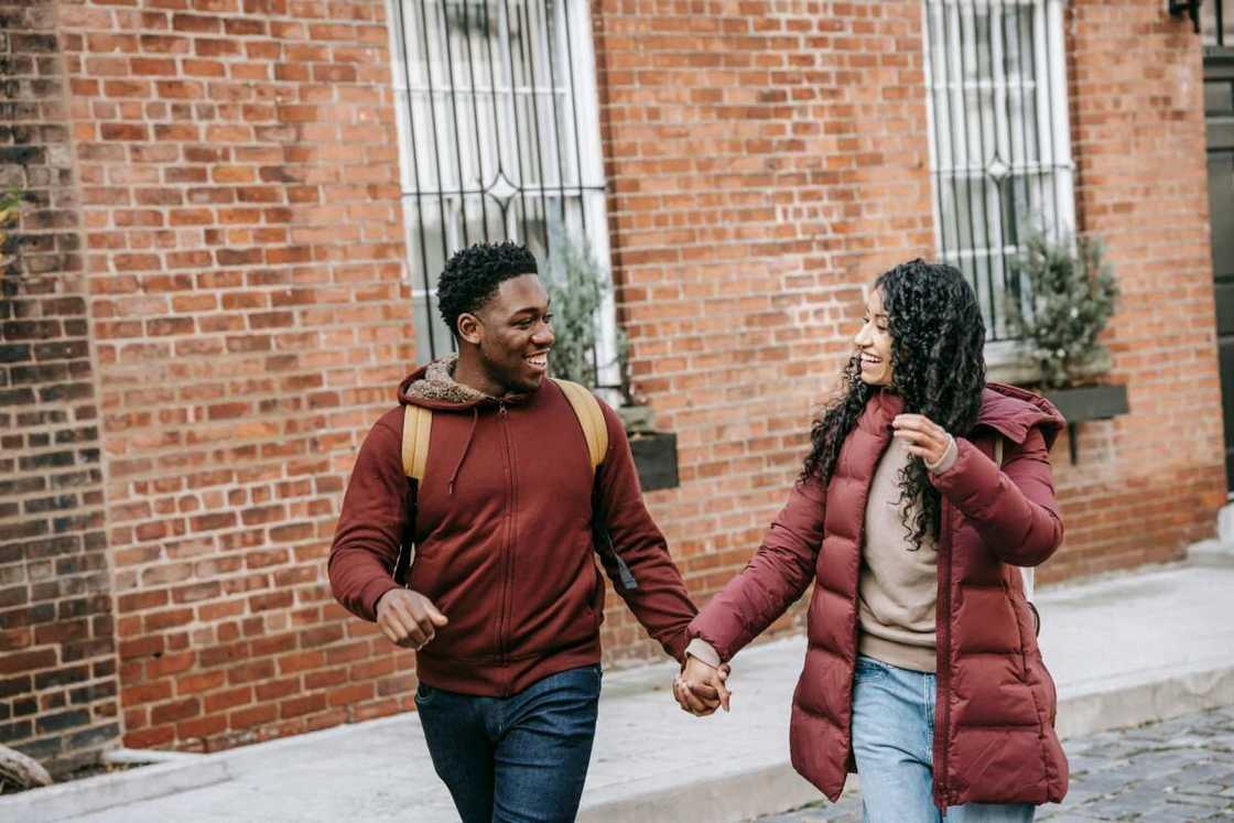 A couple holding hands while walking on a pavement.