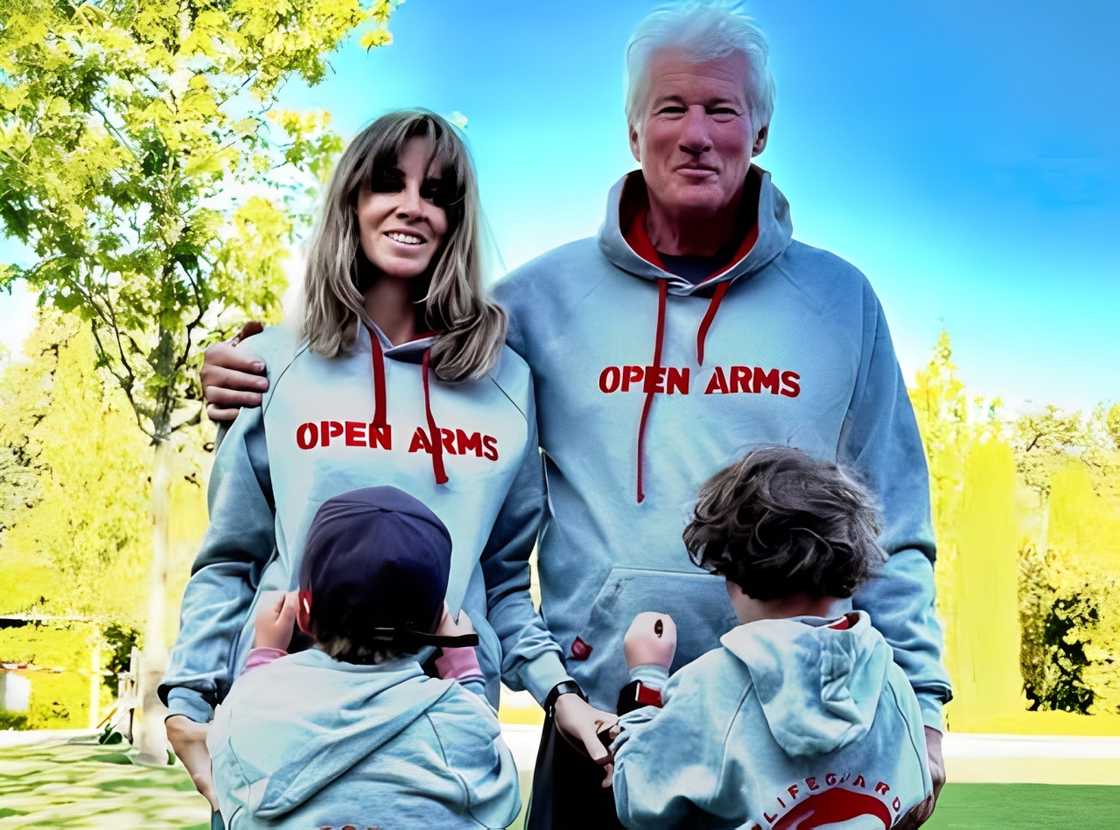 Richard Gere posing in a grey Open Arms hoodie with his wife, Alejandra Silva, and their children.