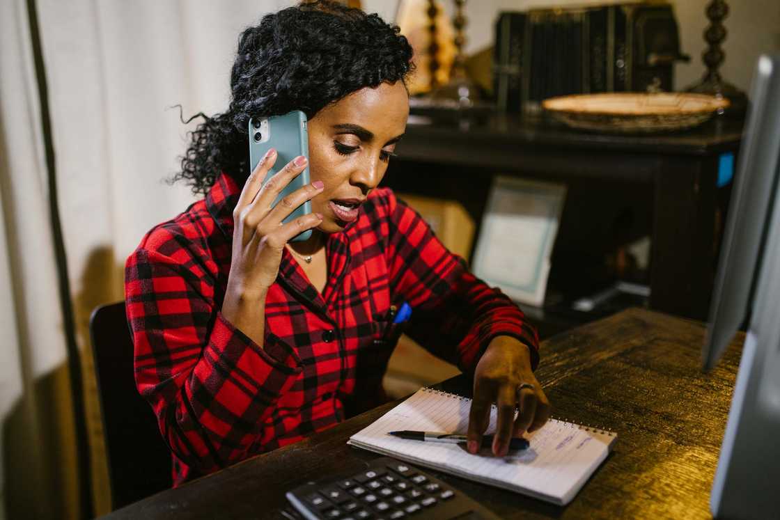A woman talks on the phone while writing in a notebook.