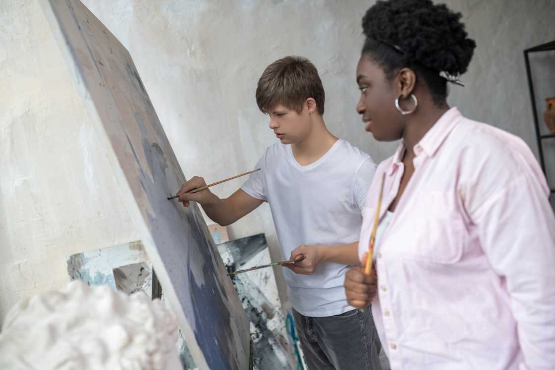 A boy standing near the easel and drawing with great involvement