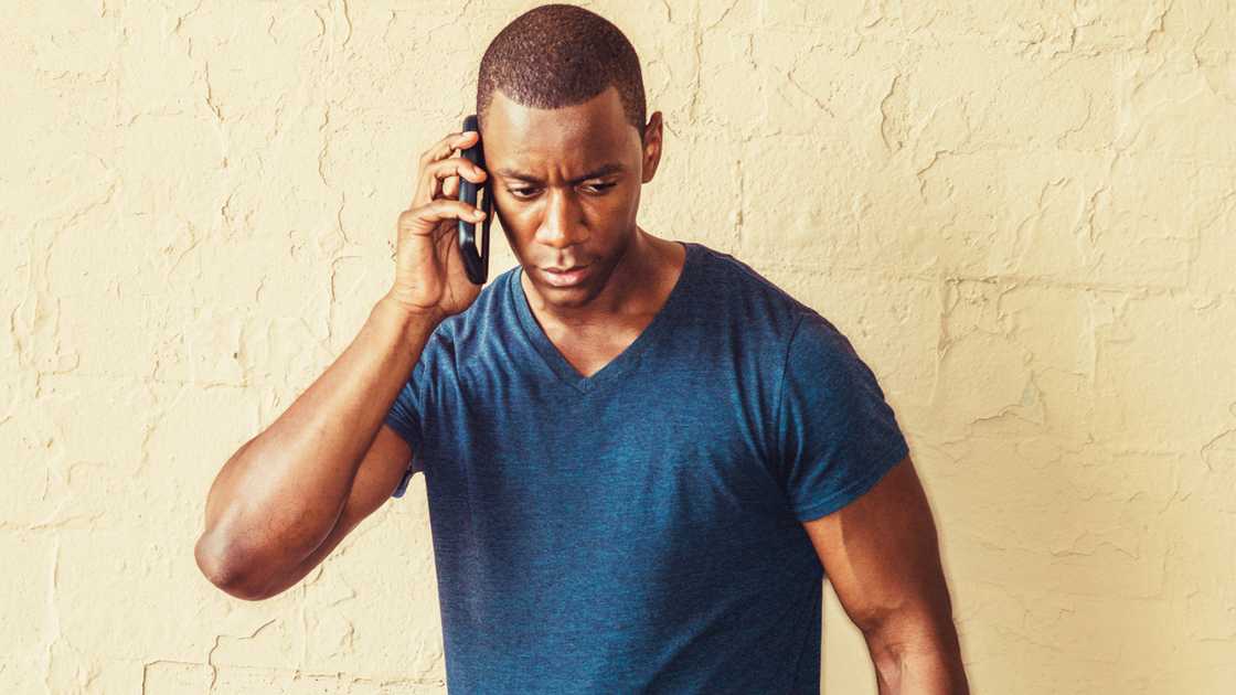 A man wearing a blue V-neck T-shirt talking on cell phone.