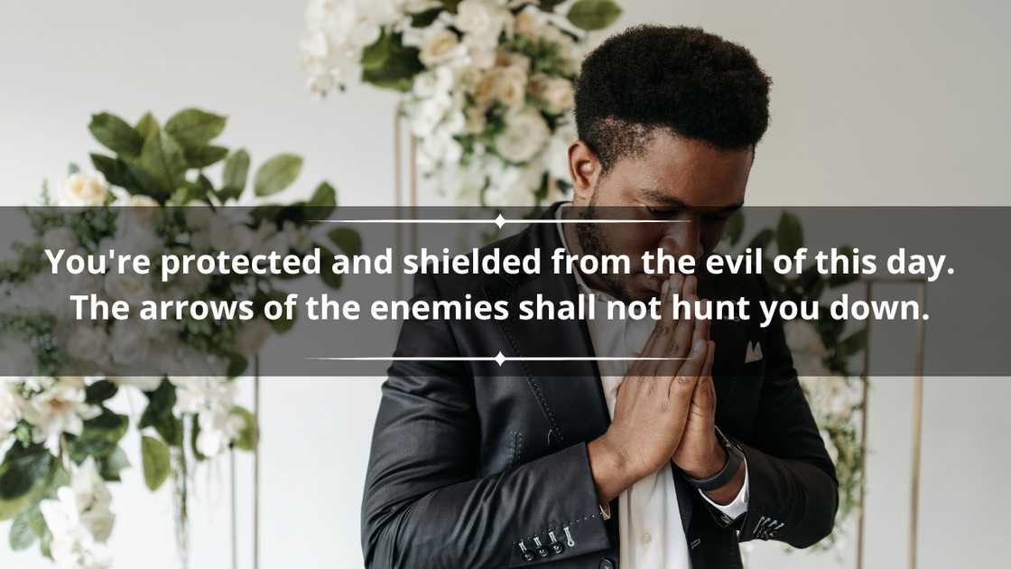 A black man in a black suit jacket is holding his hands together in prayer