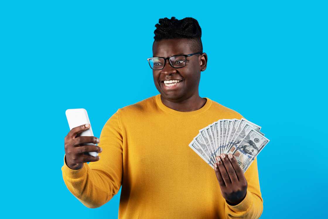 A man smiles holding dollar currency looking at his phone A man smiles holding dollar currency looking at his phone