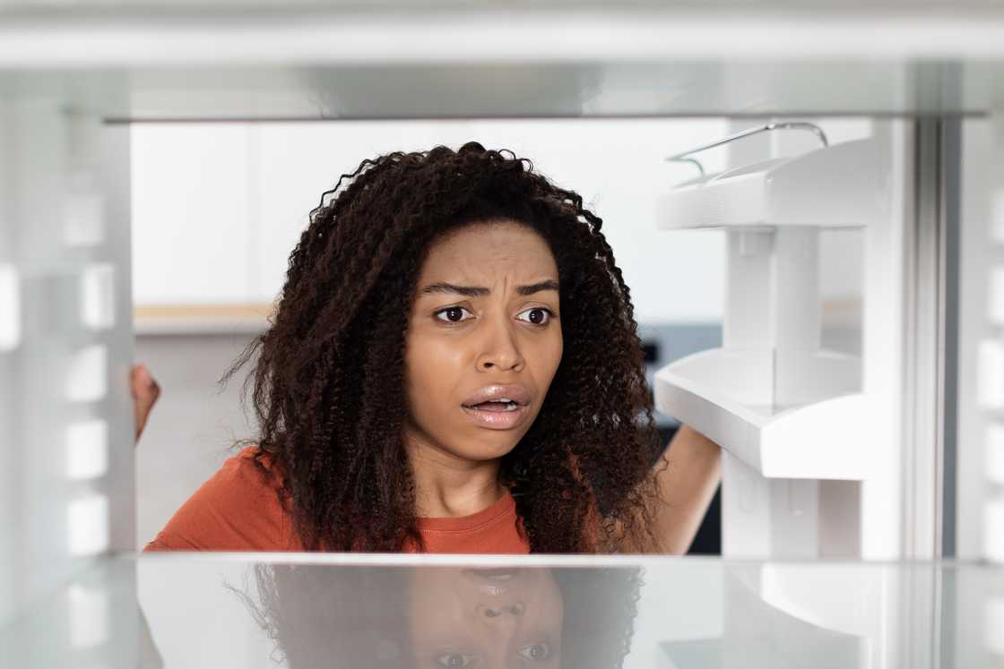 A frustrated, shocked young woman opening the refrigerator door A frustrated, shocked young woman opening the refrigerator door